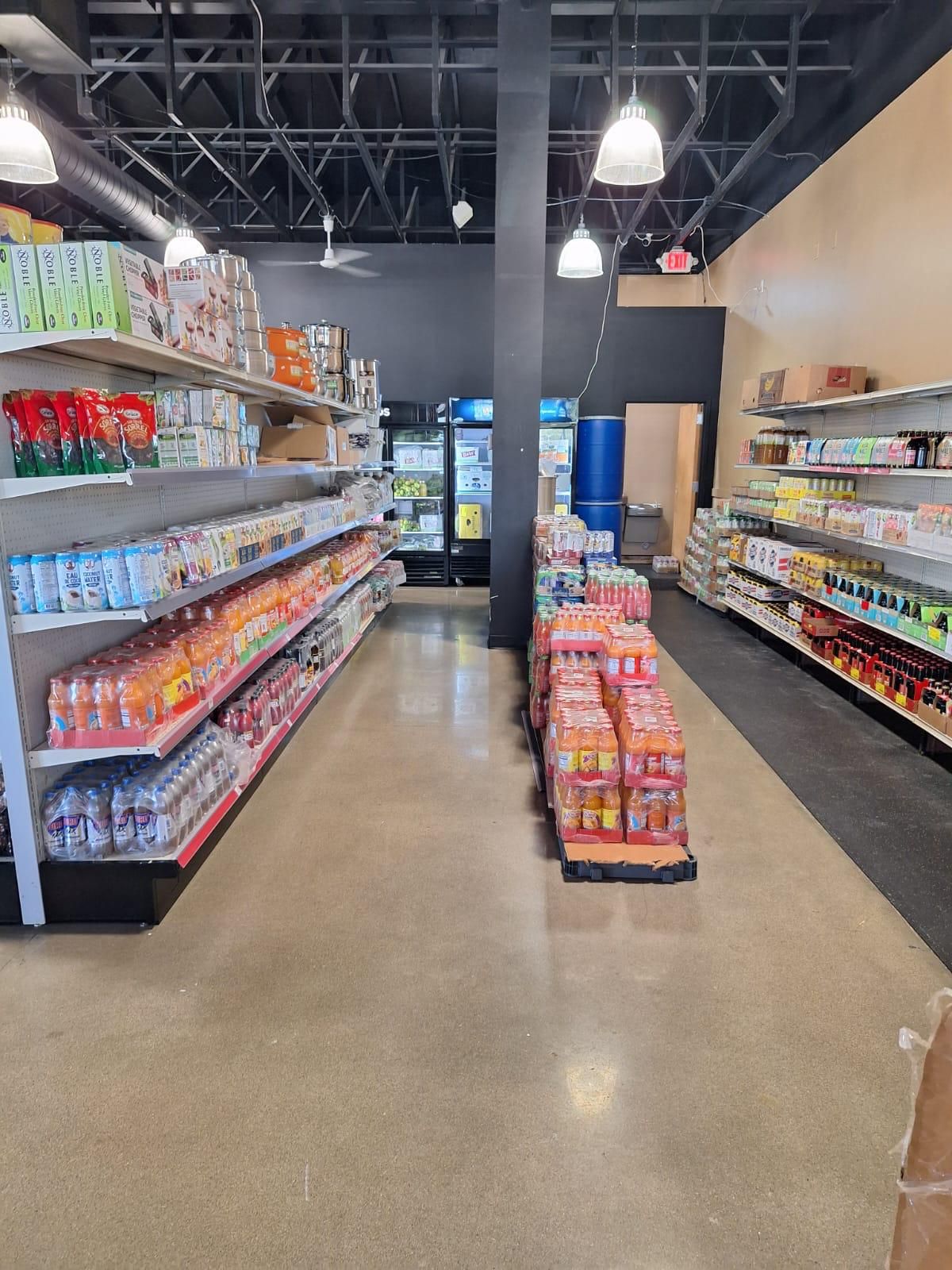 Looking down the beverage aisle at JNS Food Market past the coolers, juice pallets, and shelves of imported sauces and snacks.