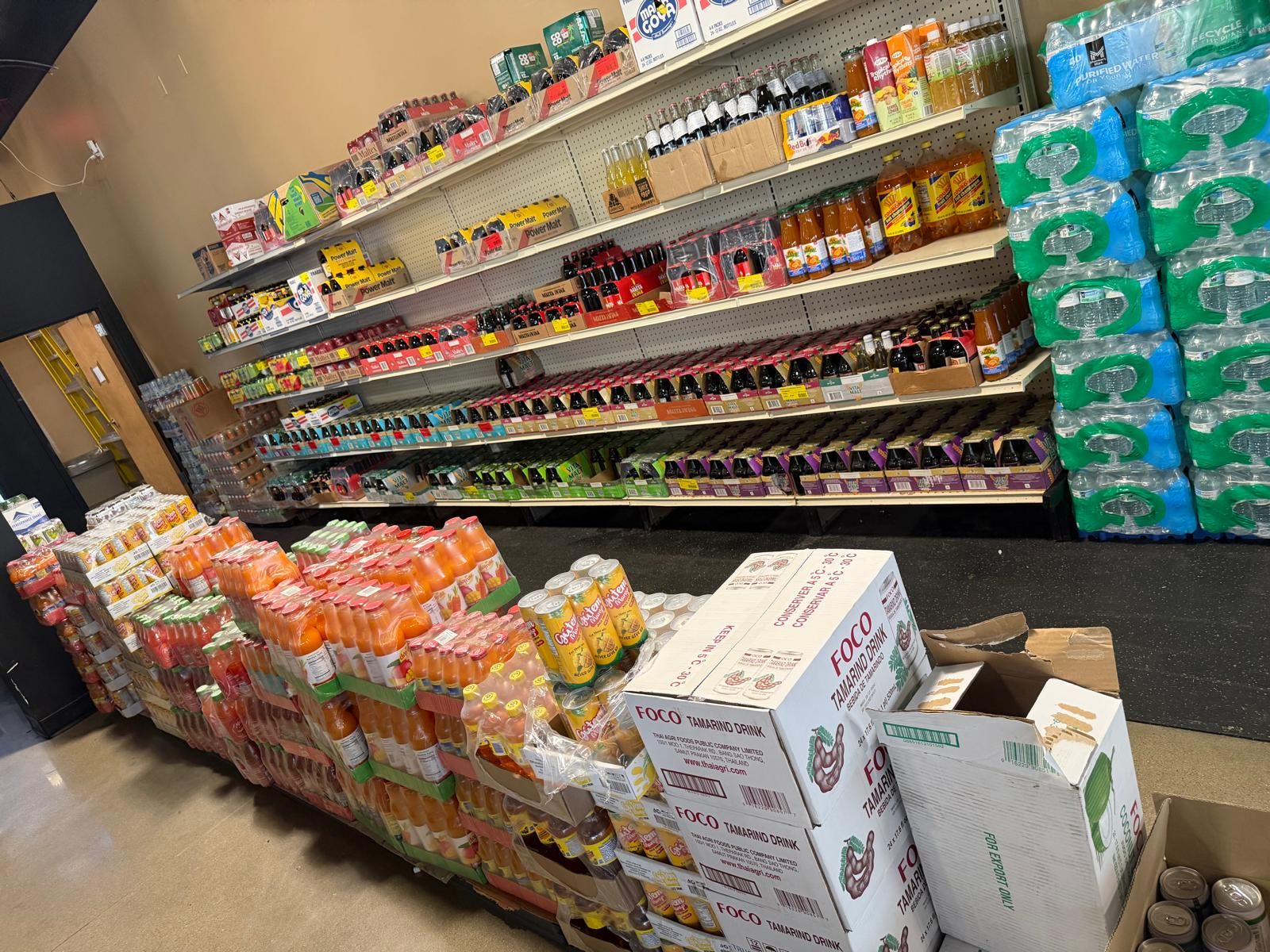 The drink wall at JNS Food Market — tropical juices, malta, imported sodas, cases of tamarind drink, and pallets of bottled water.