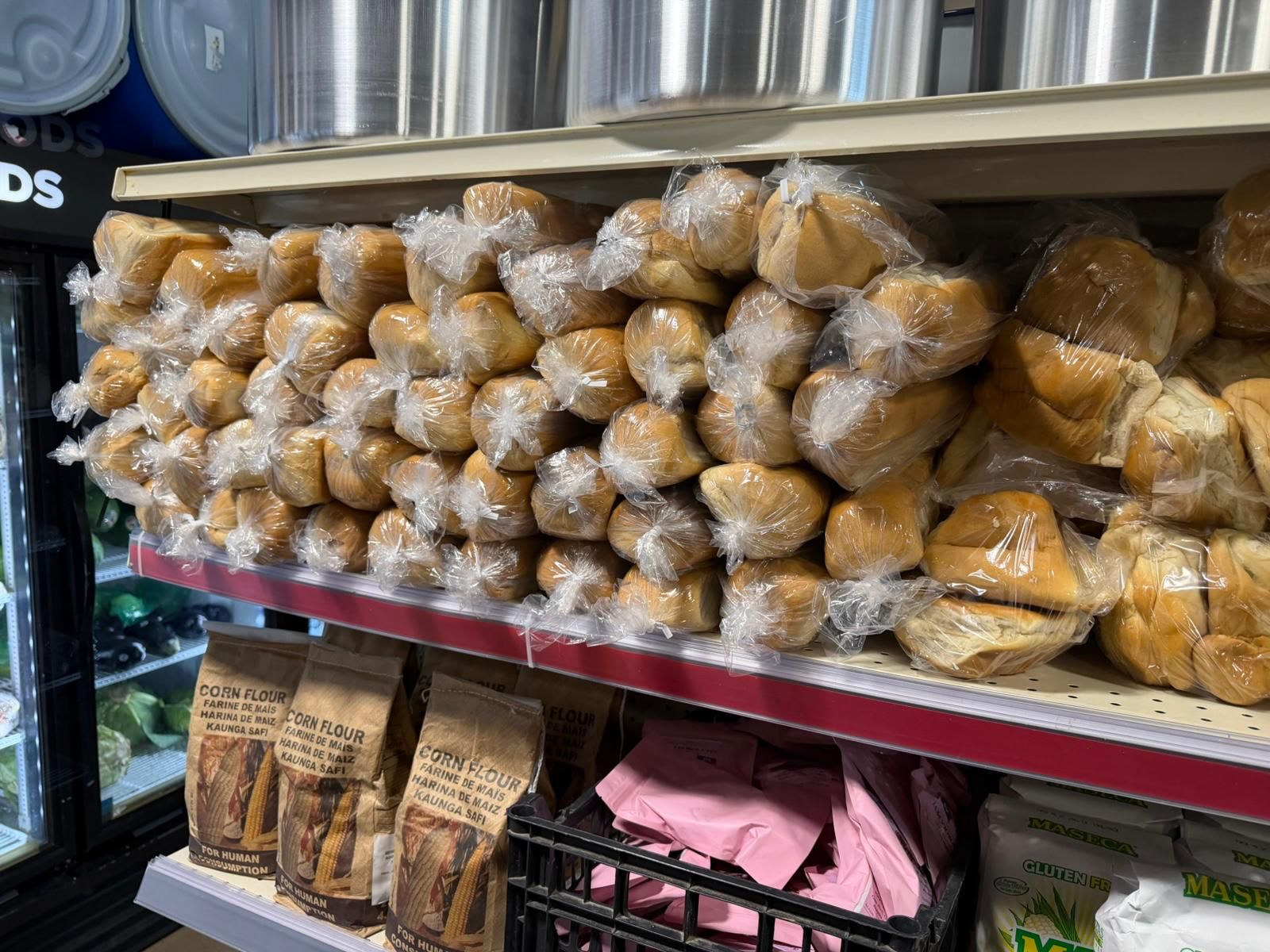 Bagged loaves of fresh Haitian bread on the shelf at JNS Food Market, with corn flour and maseca stacked underneath.