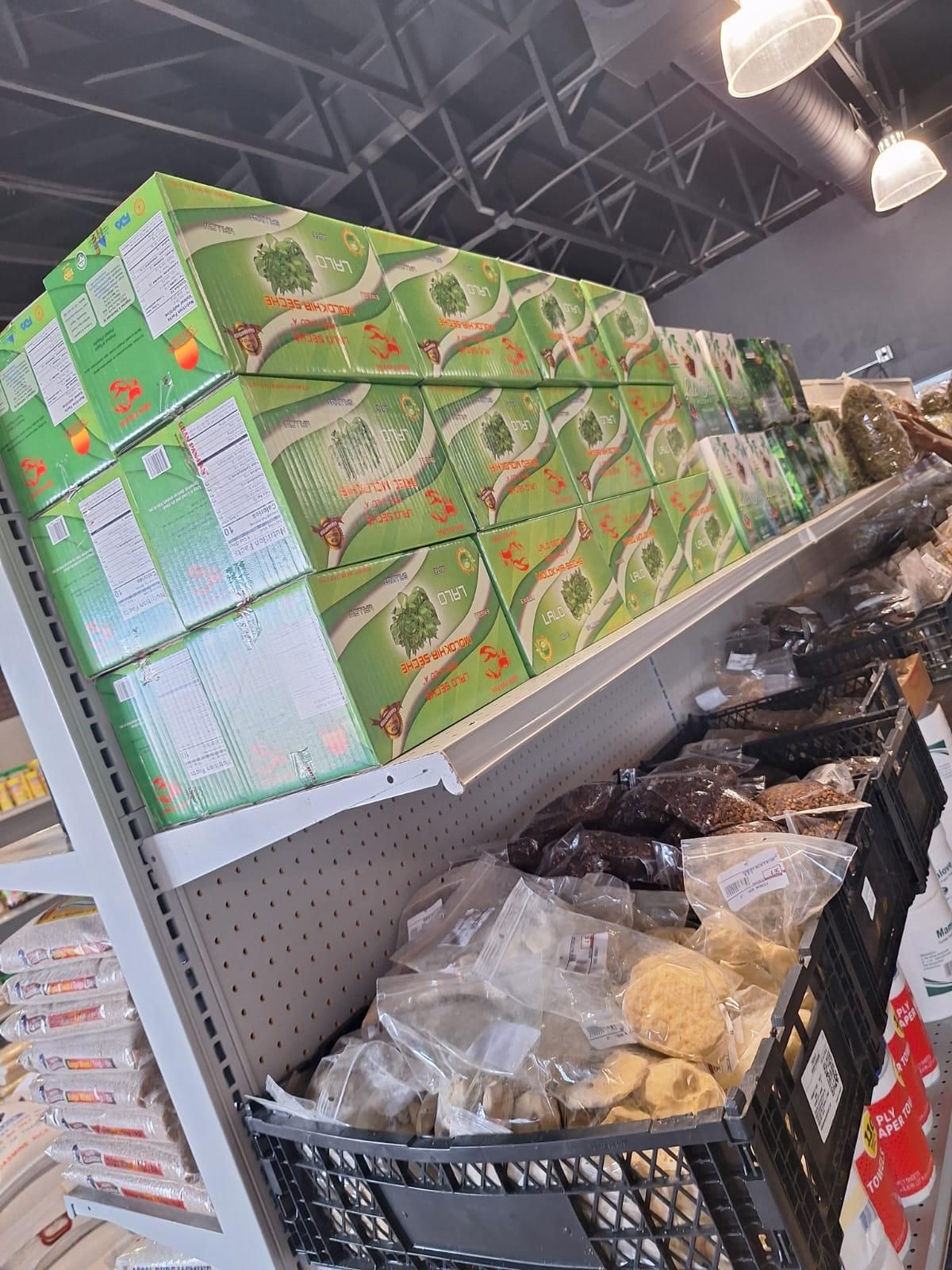 Cases of dried herbs and packaged Haitian staples stacked at JNS Food Market, with crates of specialty dry goods on the shelves below.