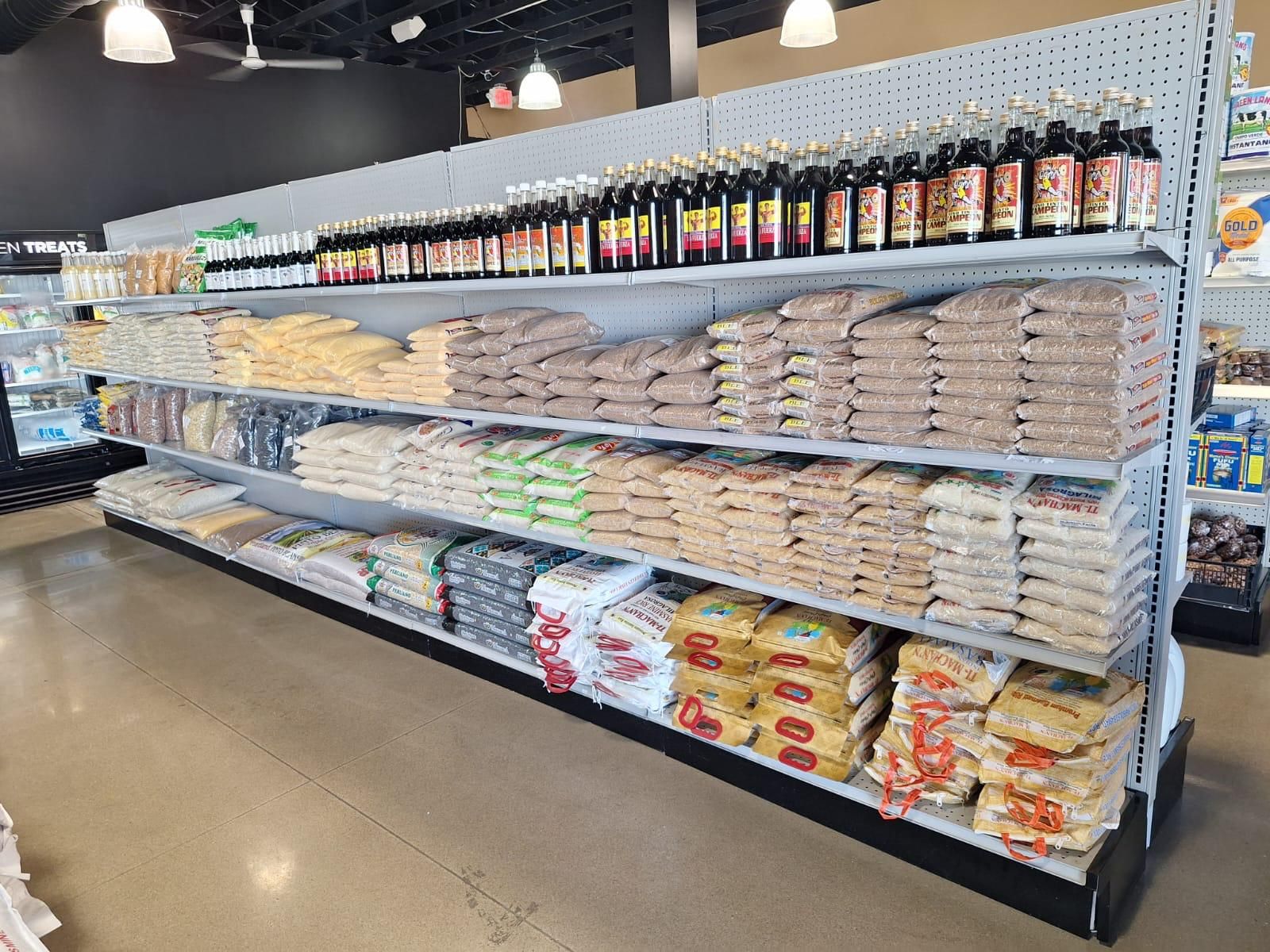 Shelves of bagged grains, cornmeal, and dried beans at JNS Food Market, topped with rows of Kola champagne and imported soft drinks.